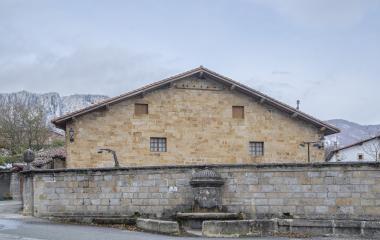 Casa tradicional de piedra en Ziordia con fuente frontal y muro de piedras delante.