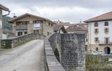 Puente medieval de piedra sobre el río en Zubiri, con casas de arquitectura tradicional pirenaica al fondo.
