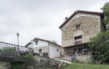 Casas de piedra tradicionales en Zuriain, al lado de puente con barandilla de metal y vegetacion.