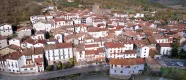 Vue aérienne de Burgui avec des maisons d'architecture traditionnelle, une église et une rivière traversant le village entre des montagnes boisées.