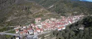 Vue aérienne de Garde avec des maisons aux toits rouges dispersées dans une vallée pyrénéenne entourée de forêt et de montagnes.