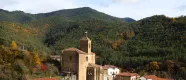 Village de Roncal avec son église, ses maisons en pierre et ses toits rouges, entouré par la forêt pyrénéenne en automne.