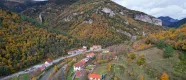 Vue aérienne d'Urzainqui avec des maisons dispersées dans une vallée pyrénéenne entourée de forêt en automne et de falaises de roche calcaire.